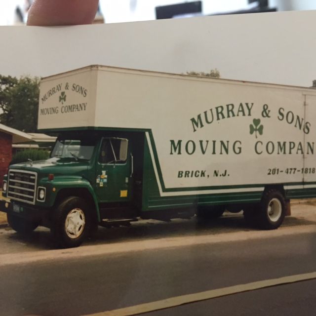 Green Murray & Sons moving truck parked on a street, with white cargo box and dark cab.
