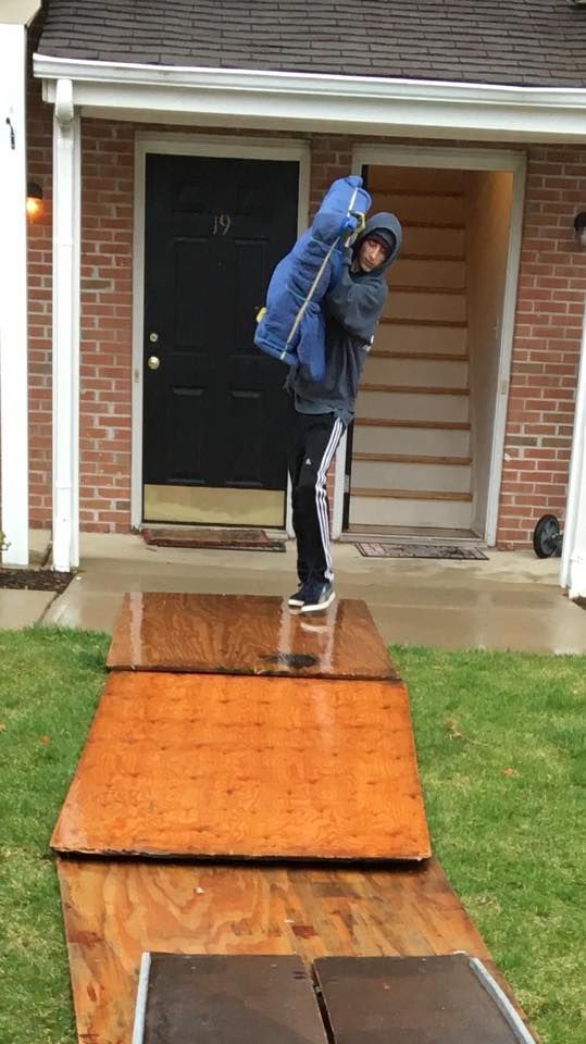 Person balancing on a wet wooden ramp outside a brick house