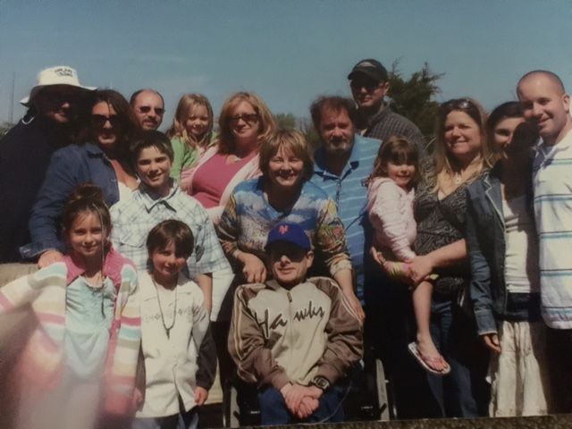 Group of people posing outdoors in a sunny field, smiling for a family-style photo.