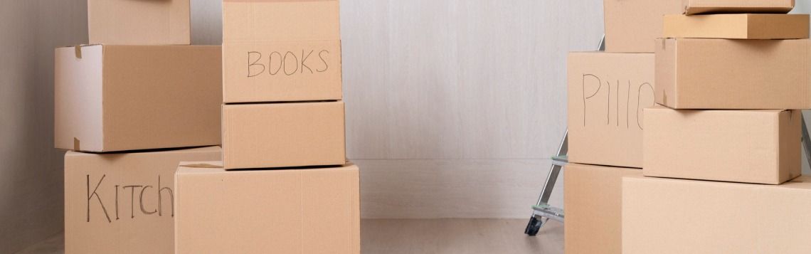 Cardboard moving boxes stacked in a room, some labeled for kitchen and books.