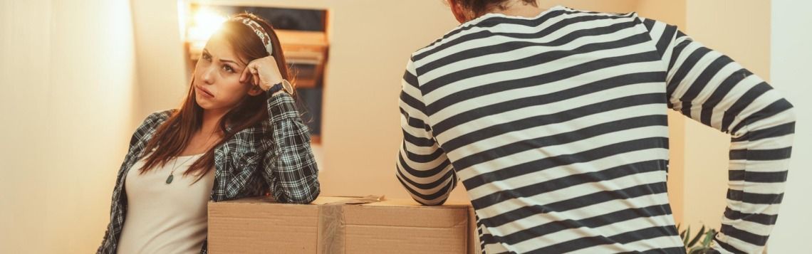 Two people in a hallway, one leaning against a box, another in a striped shirt beside it.