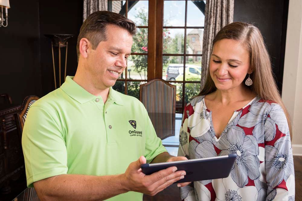 Man in green shirt shows a tablet to a woman. Both are smiling. Black background.