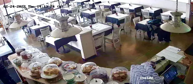 Restaurant interior with baked goods on display; tables with blue tablecloths, a server behind a counter.