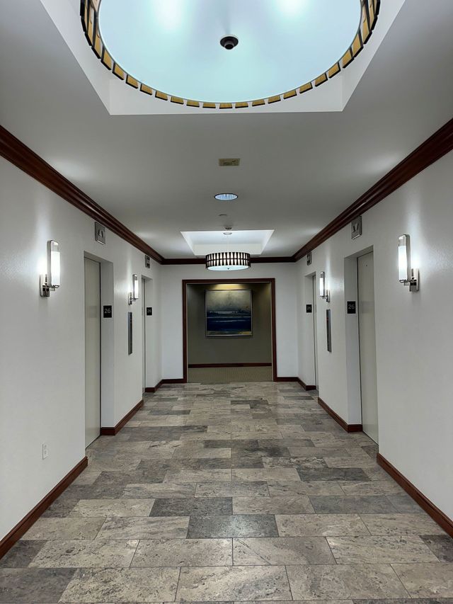 Modern hotel hallway with white walls, stone floor, sconces, and a circular ceiling opening