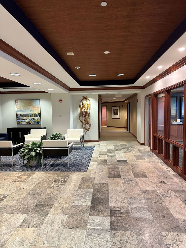 Spacious office lobby with stone floor, wood ceiling, white seating, and hallway doors.