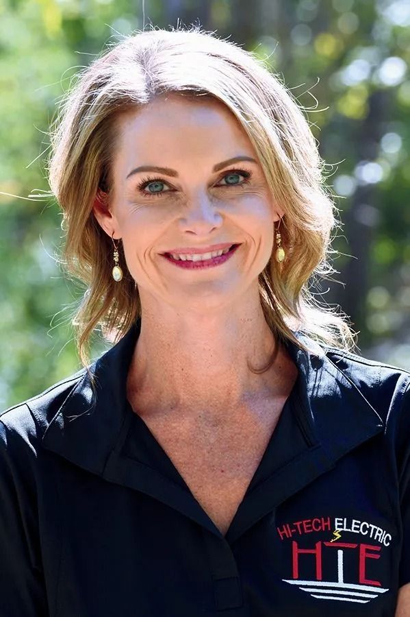 Woman with blonde hair smiles, wearing black shirt with 
