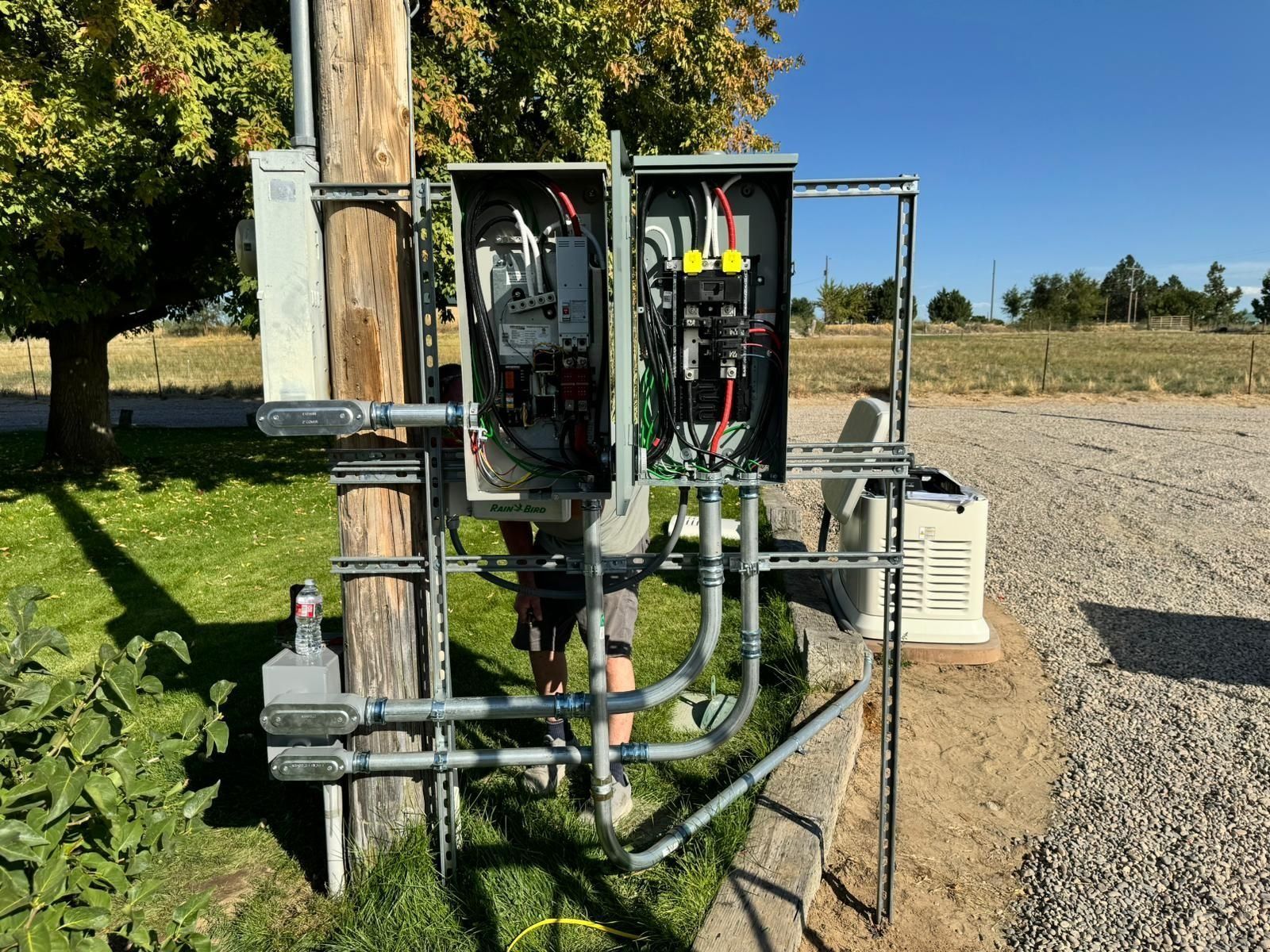 Electrical boxes mounted on a utility pole with conduit, outdoors on a sunny day.