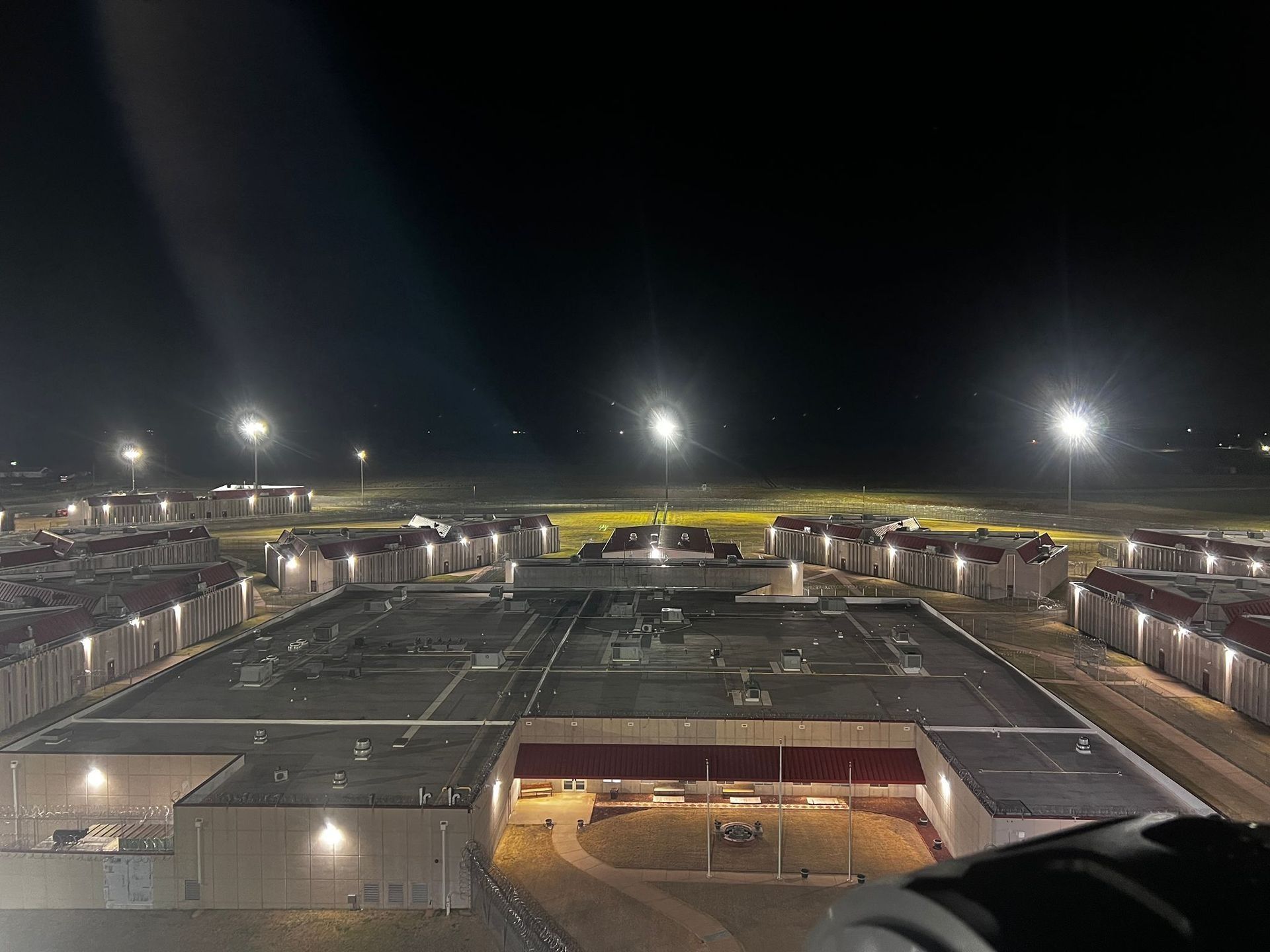 Nighttime aerial view of a prison with lit buildings and outdoor lights against a dark sky.