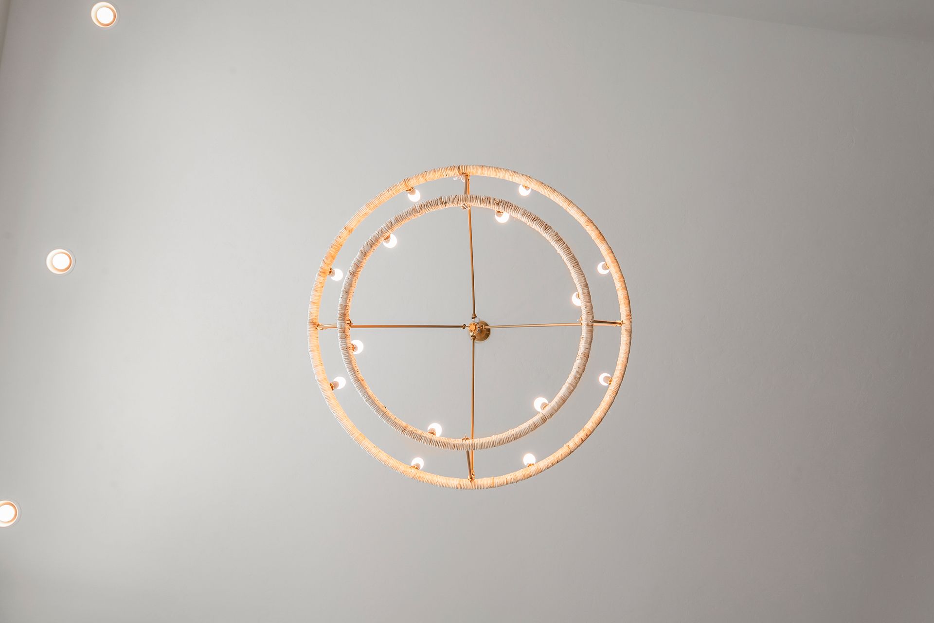 A circular gold chandelier with lights against a light gray ceiling, other ceiling lights are visible.