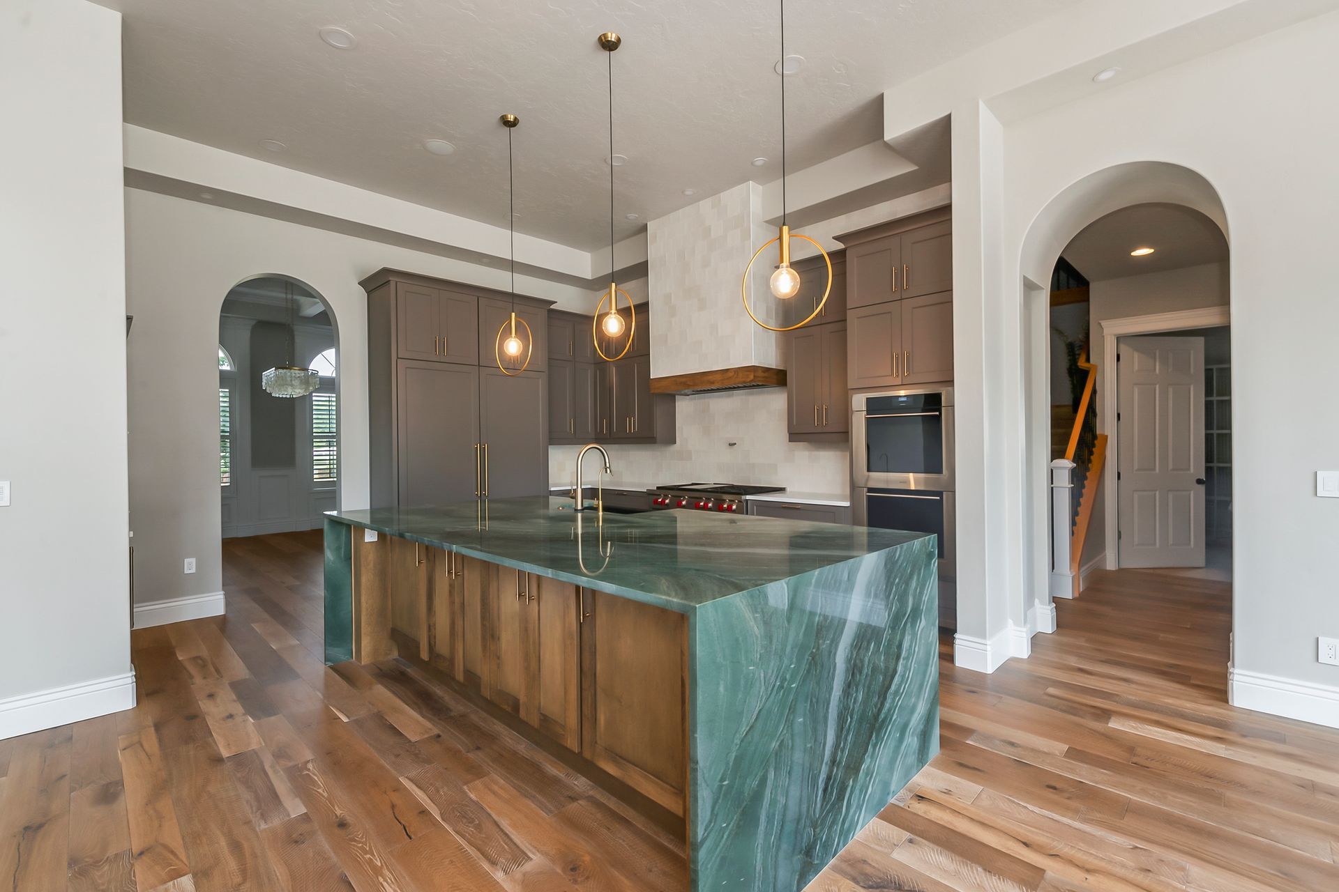 Spacious kitchen with a green island, gray cabinets, wooden floors, and arched doorways.