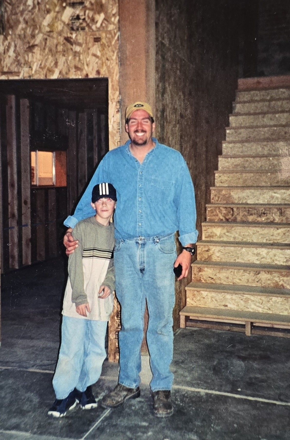 A man and a child stand inside a building under construction. The man has his arm around the child.