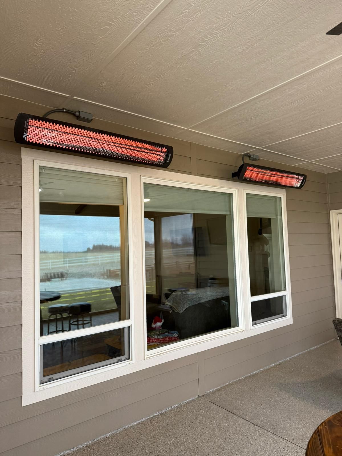 Two red infrared heaters mounted above a window on an outdoor porch, providing warmth.