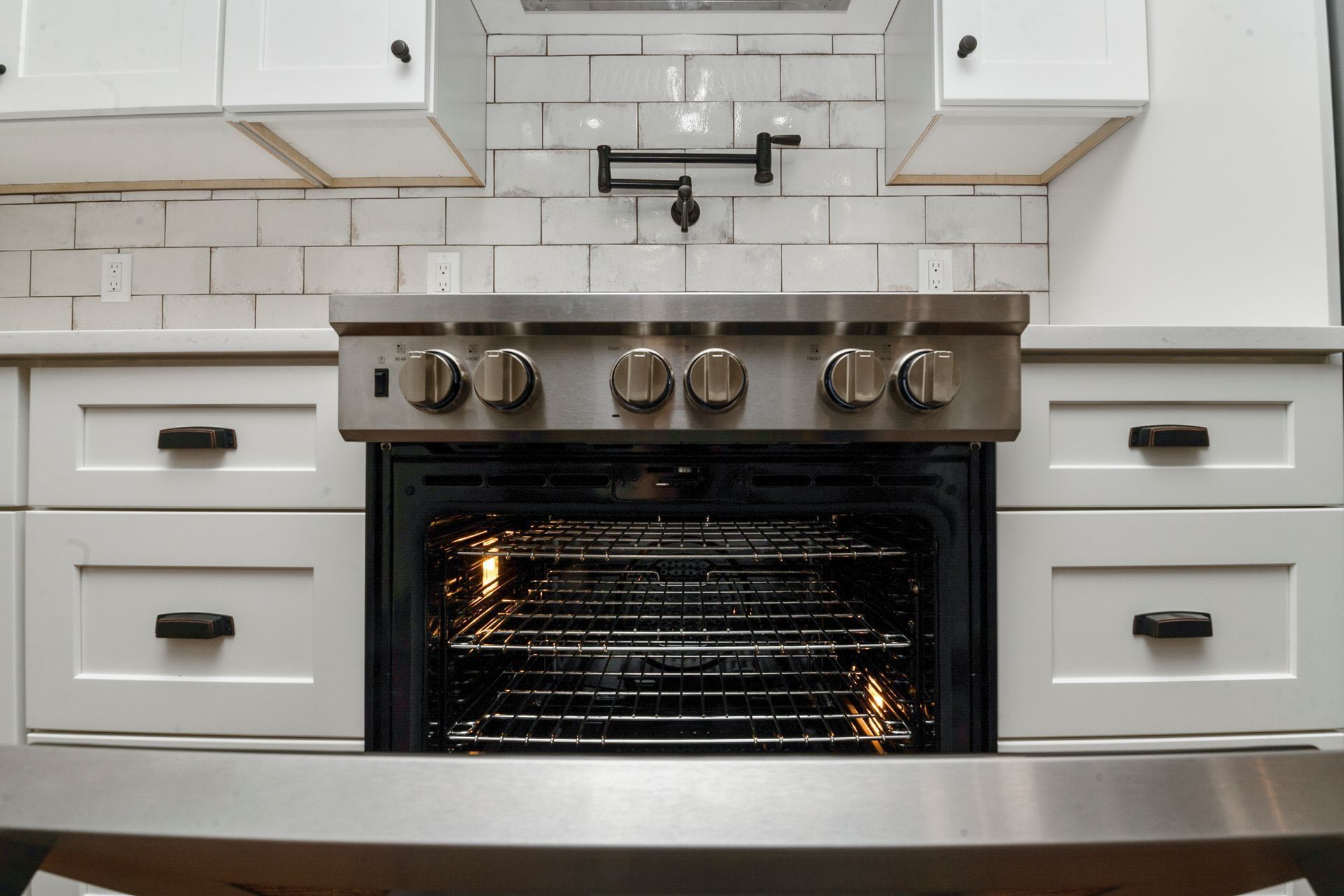 A stainless steel oven with an open door in a kitchen with white cabinets and a subway tile backsplash.