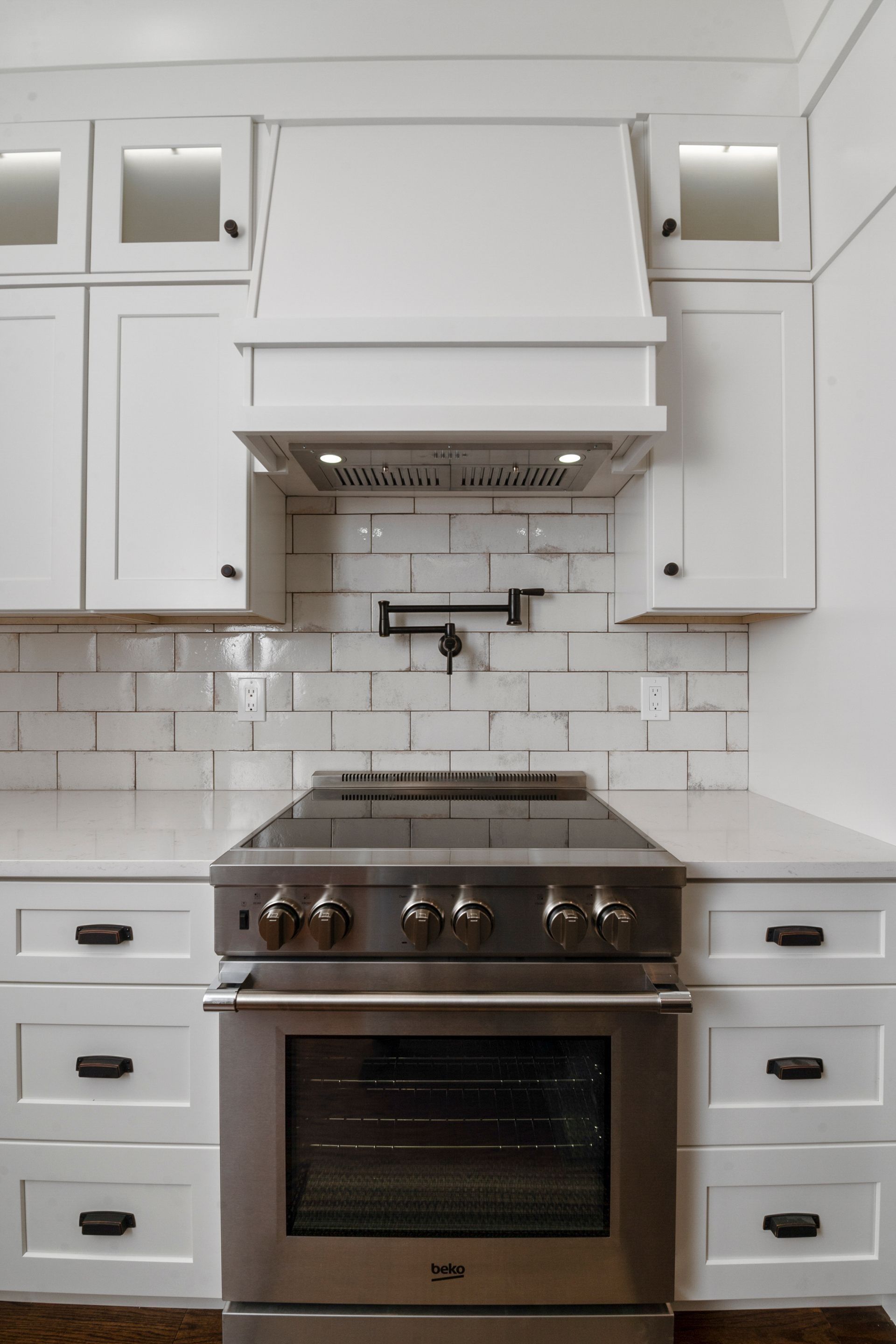 White kitchen with stainless steel range, subway tile backsplash, and overhead range hood.
