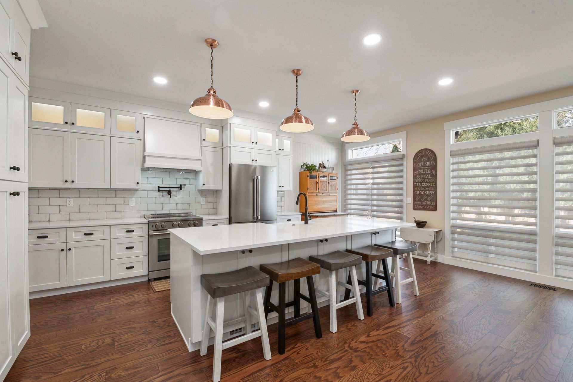 Bright white kitchen with copper pendant lights, large island, and wooden floors.
