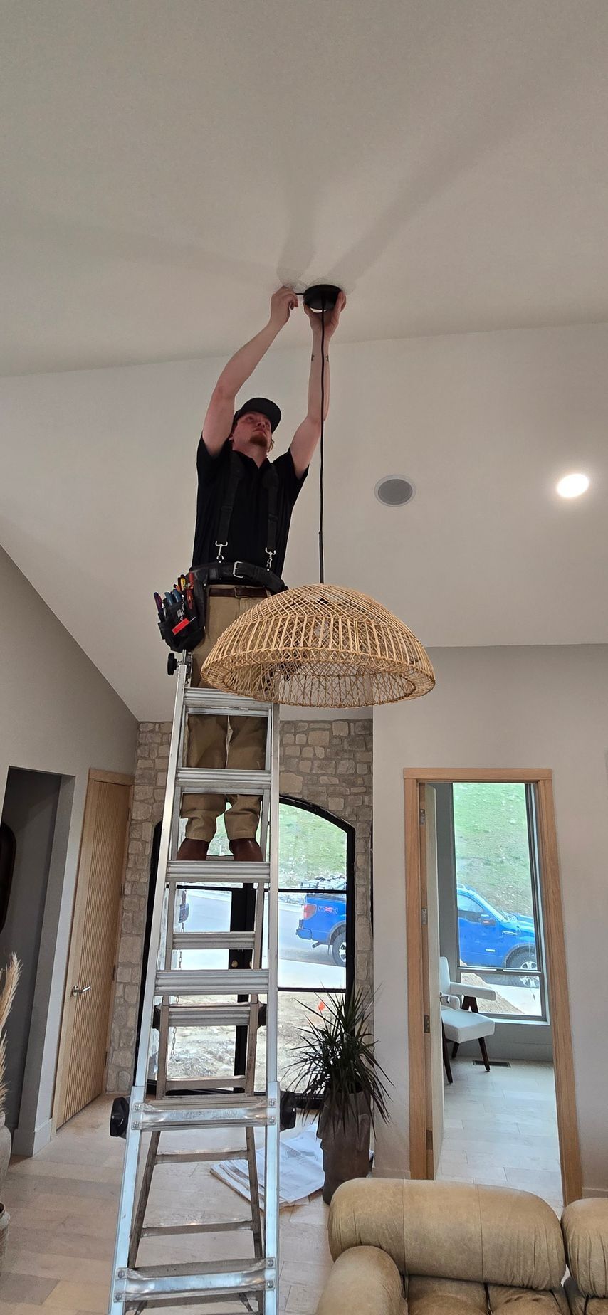 Man installing a chandelier while standing on a ladder in a living room.
