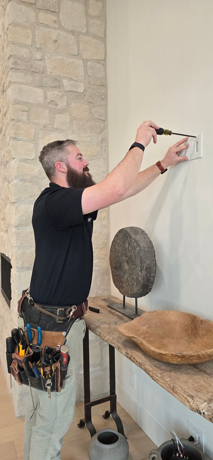 Electrician installing an electrical outlet on a wall with a stone wall to the left.