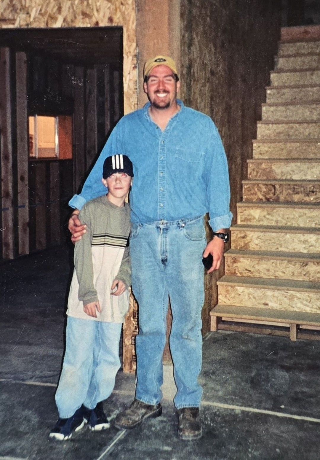 Man with arm around a boy, posing for the camera indoors, unfinished construction setting.