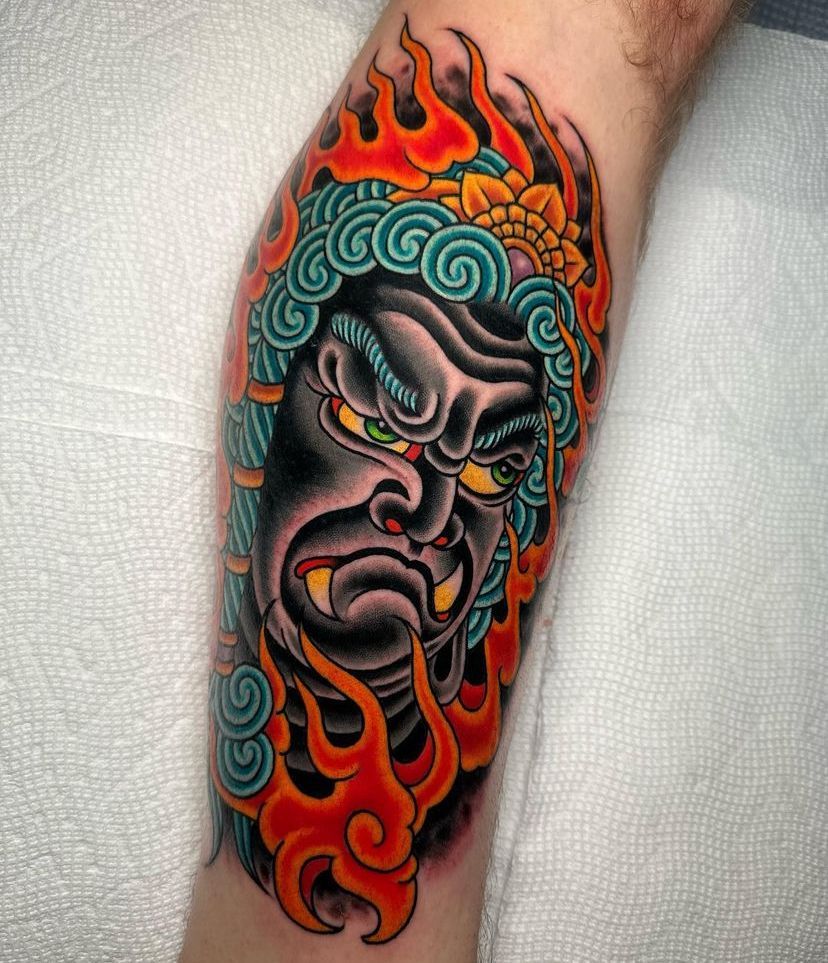 a colorful tattoo of a demon's head with flames on a person's leg