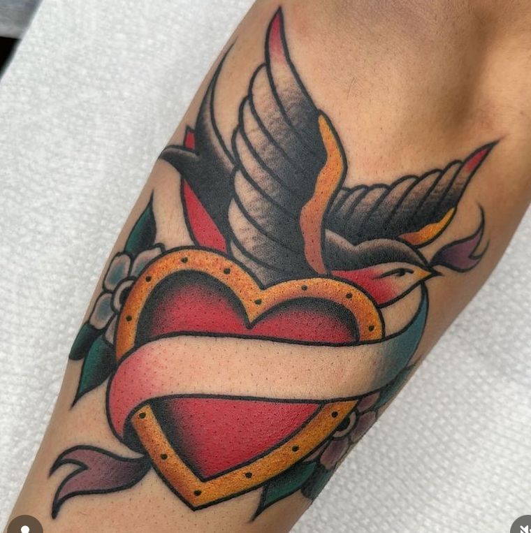 a tattoo of a bird flying over a heart with a banner around it