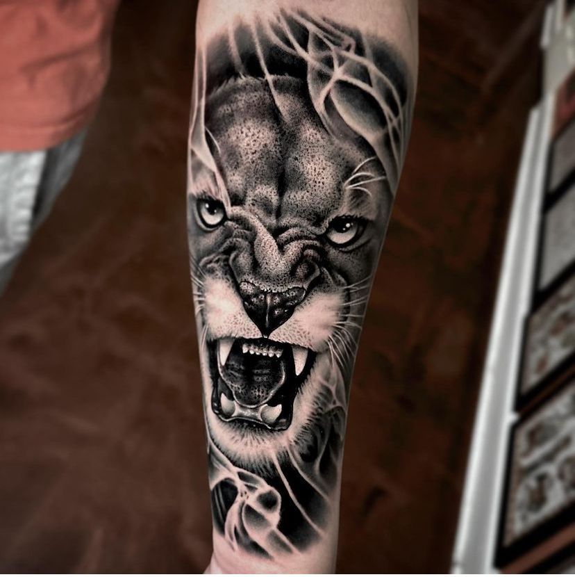 a black and white tattoo of a lion's face on a person's forearm