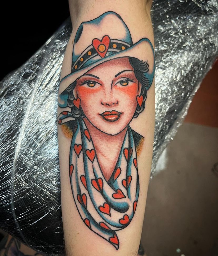 a tattoo of a woman wearing a cowboy hat and scarf with hearts on it