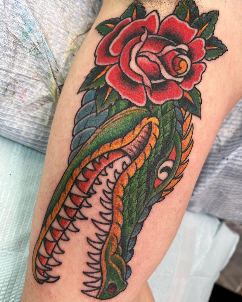 a tattoo of a crocodile and a rose on a person's arm