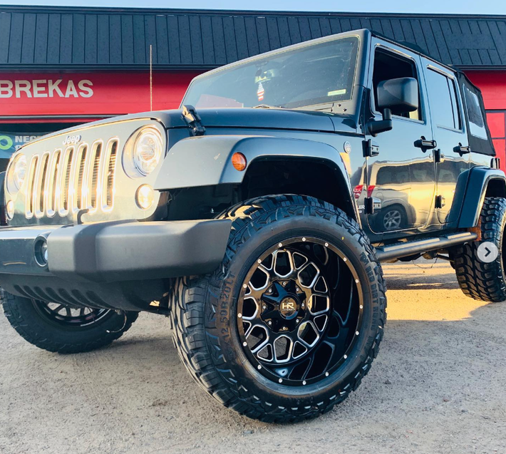 A black jeep is parked in front of a store that says brakes