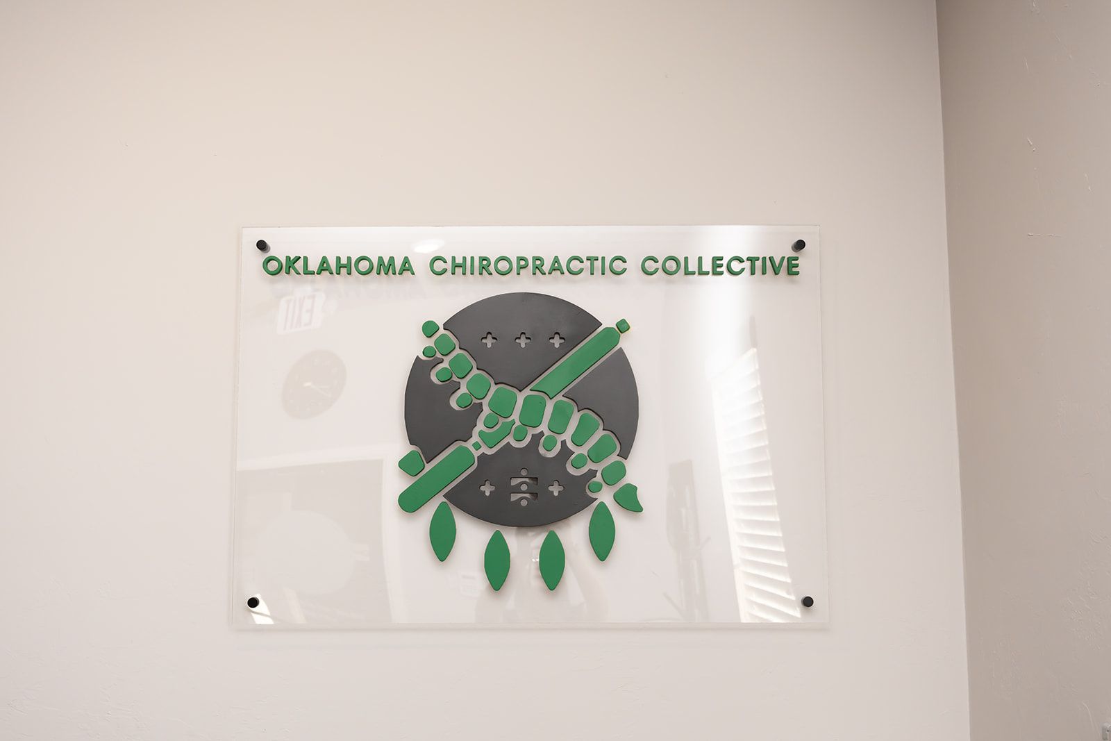 Oklahoma Chiropractic Collective sign with green logo on a white wall