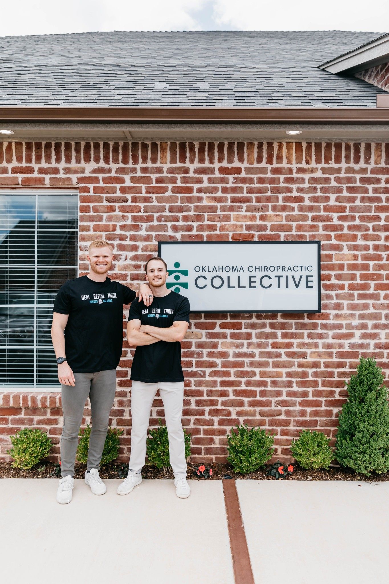 Two people standing outside a brick building beside a sign reading “Collective”