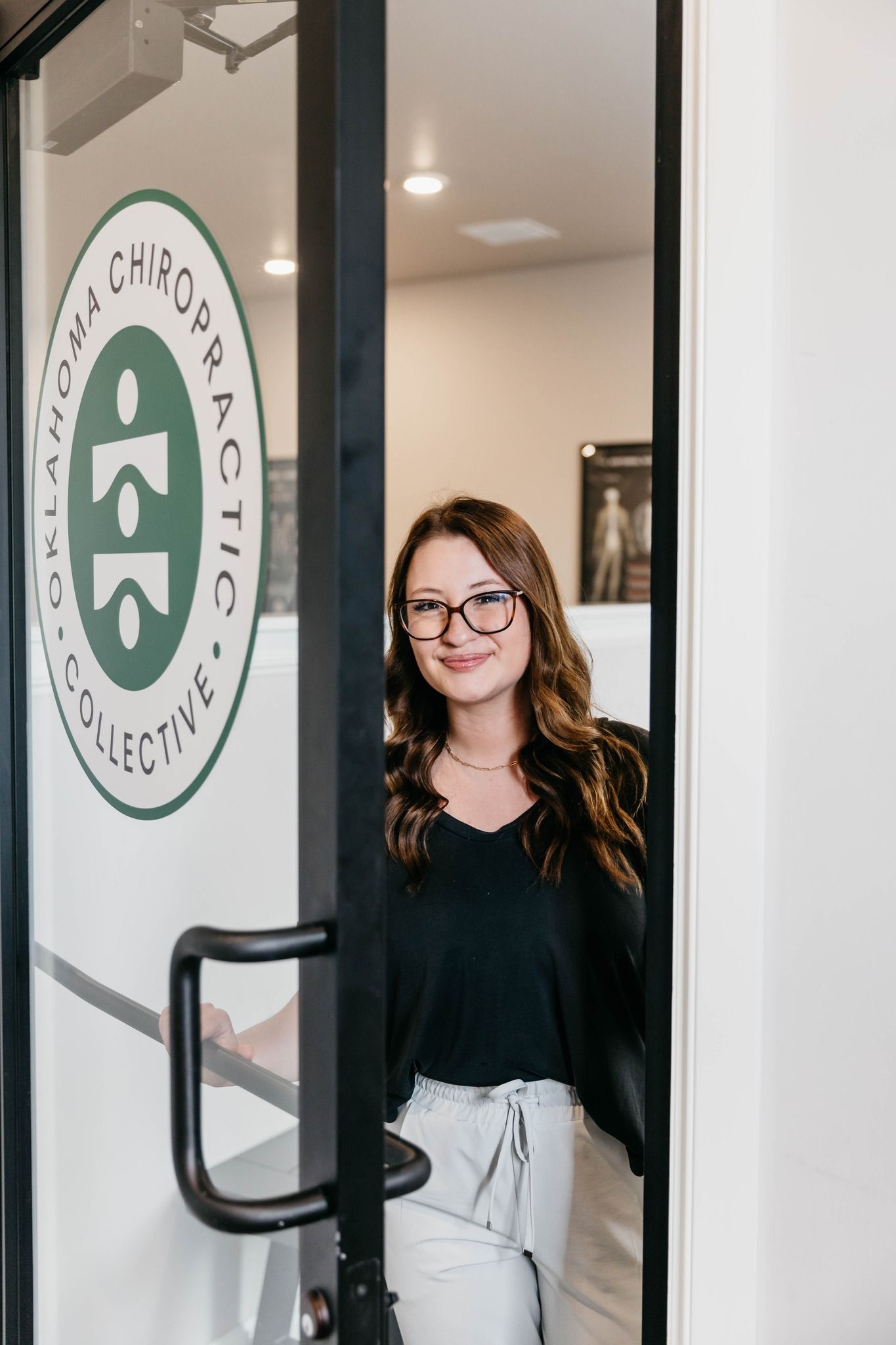 Woman standing in a doorway, smiling, with a glass door and office logo behind her