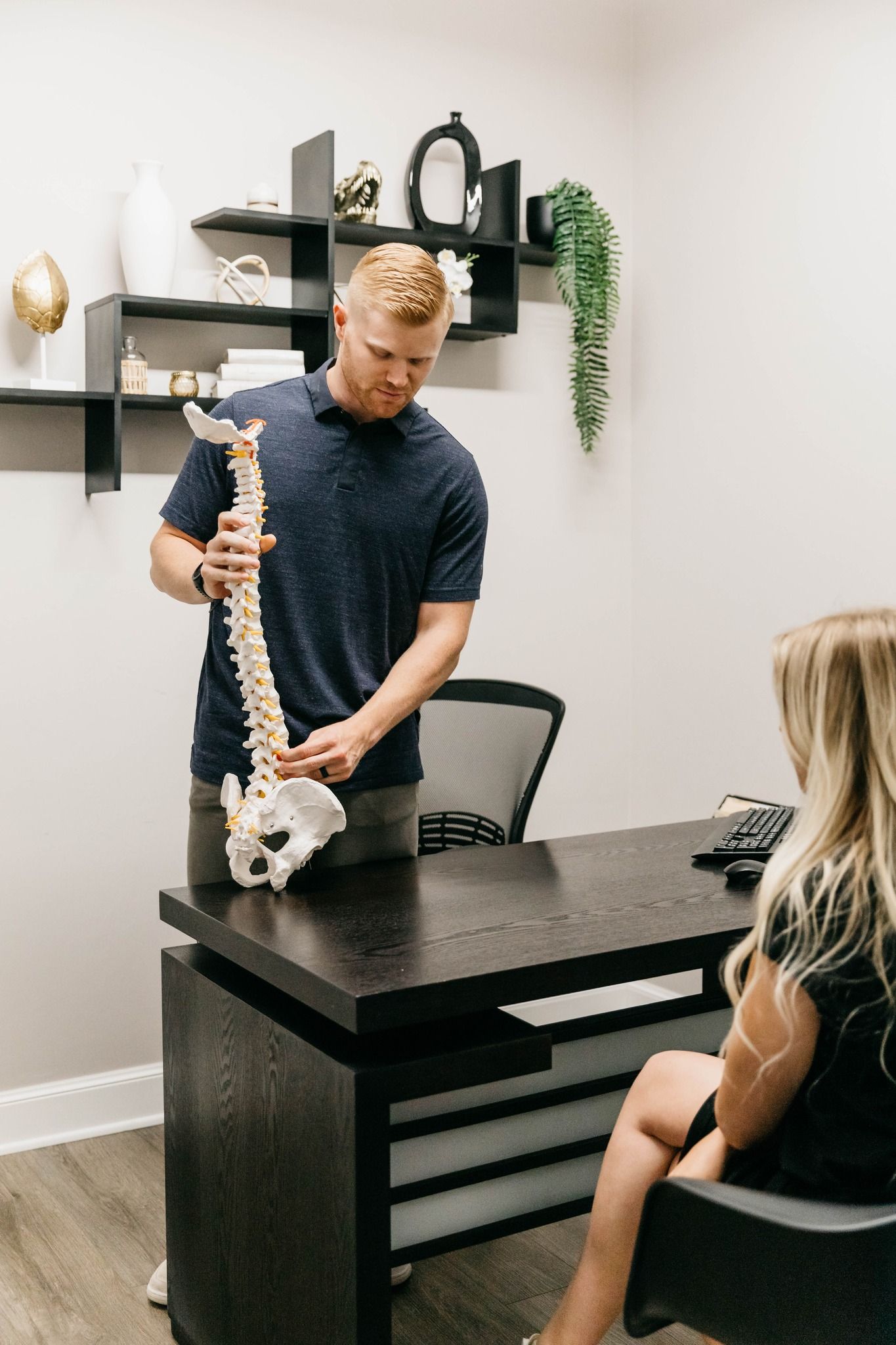 Therapist showing spine model to seated client in a small office