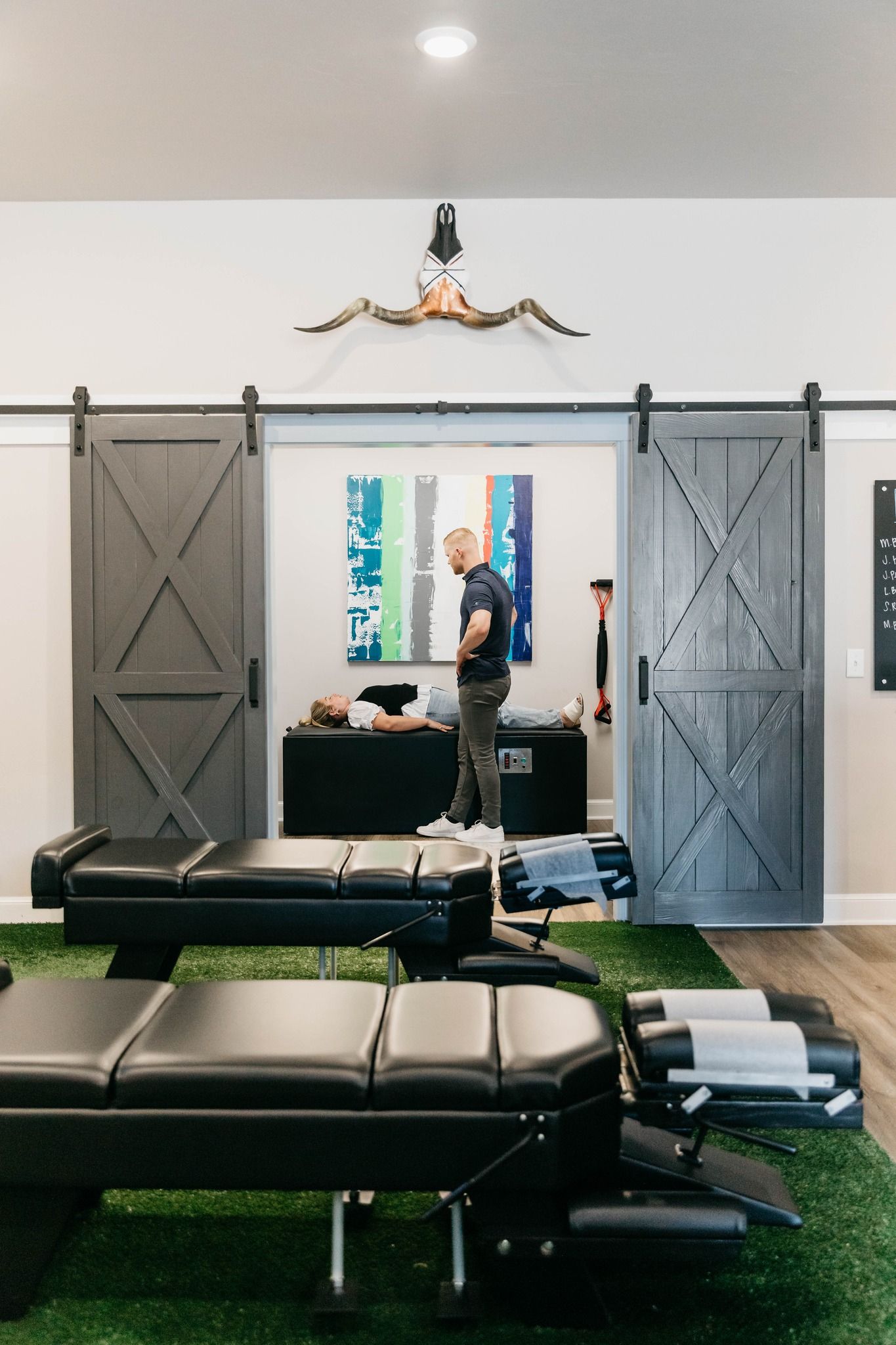 Interior of a modern gym with a person standing by a mirror, leather benches, and a wall-mounted TV