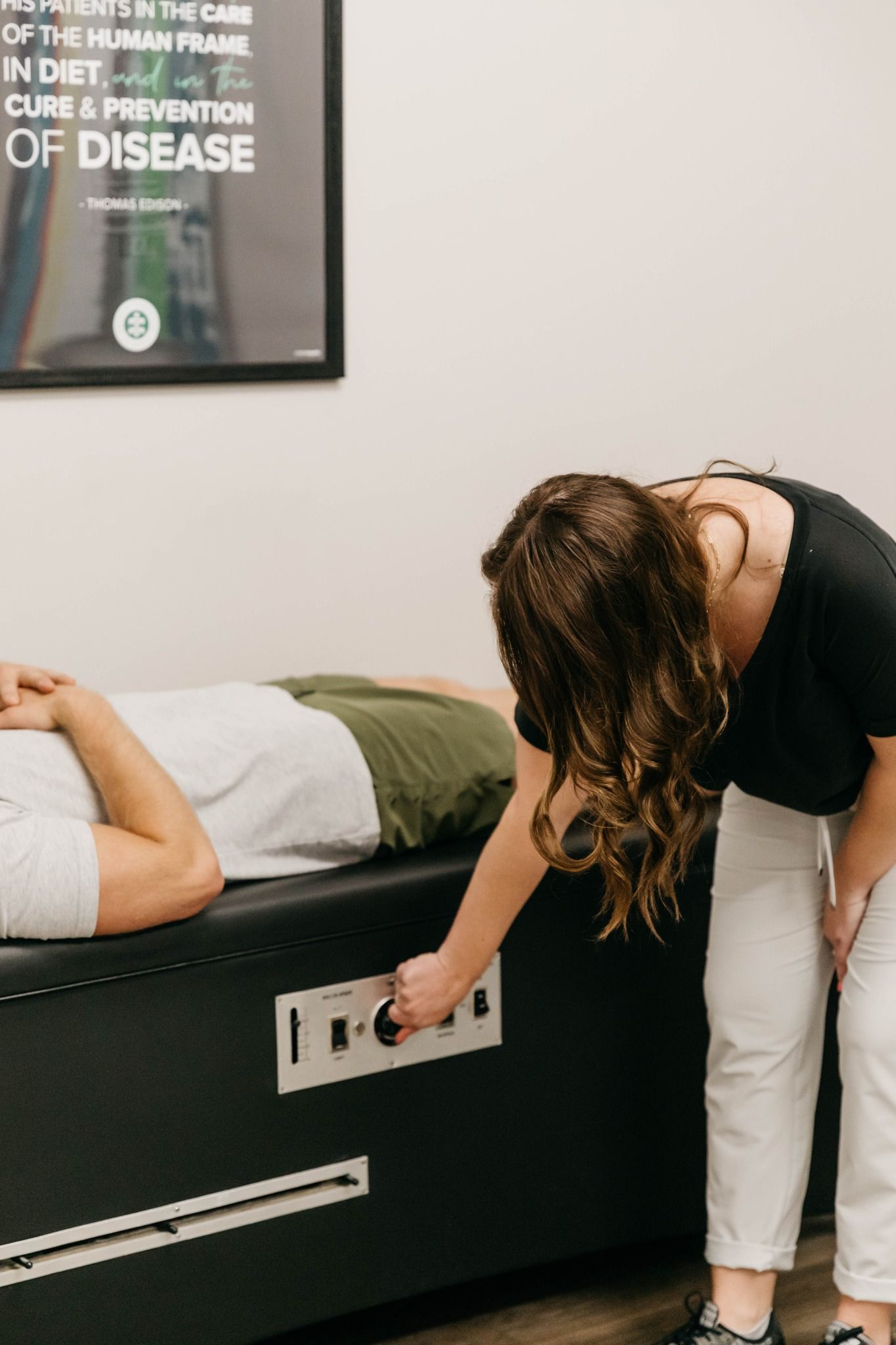 Person adjusting controls on a treatment table beside a patient in a clinical room