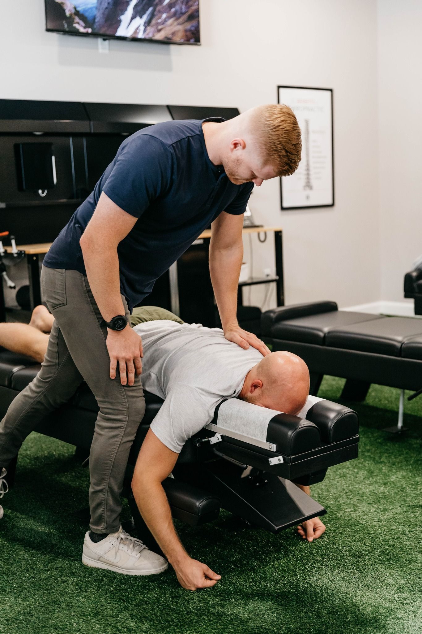 Chiropractor adjusting a patient on a treatment table in a clinic with turf flooring
