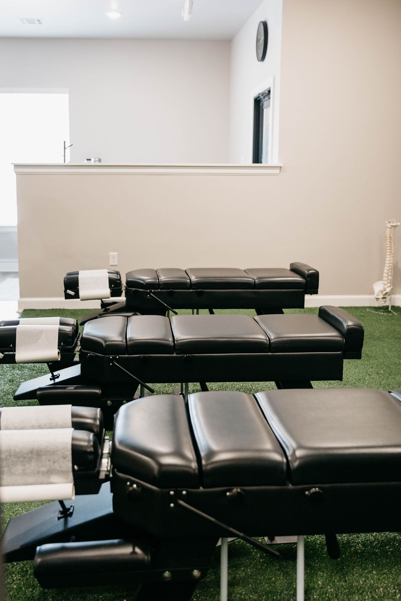 Chiropractic treatment room with black padded adjustment tables and green turf flooring