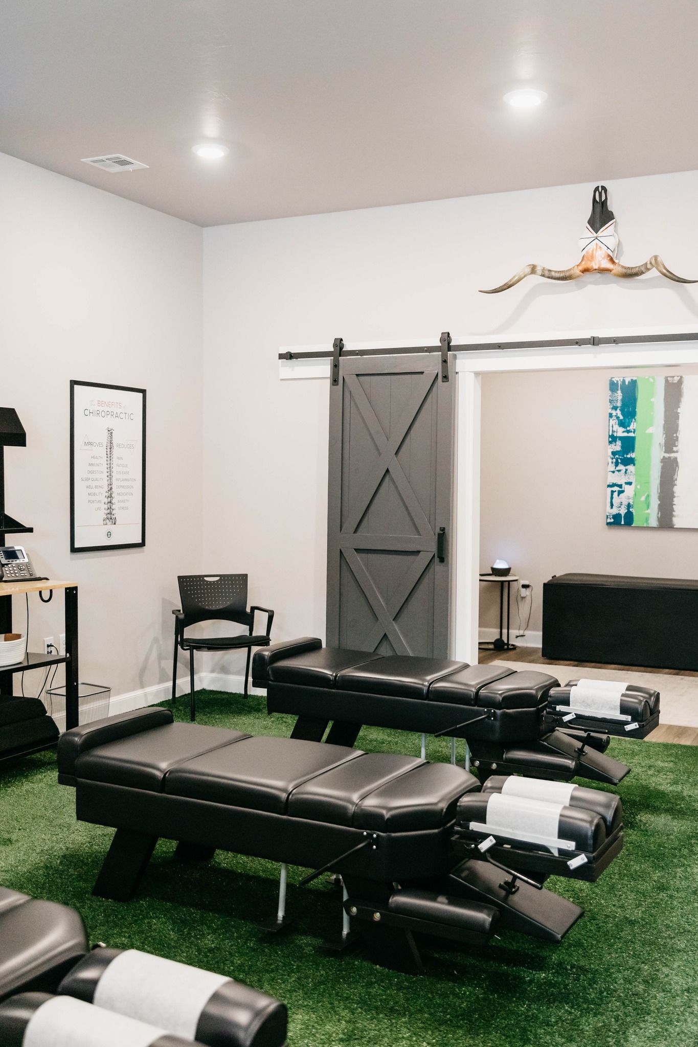 Chiropractic treatment room with black tables, wall ladder, and green turf flooring.