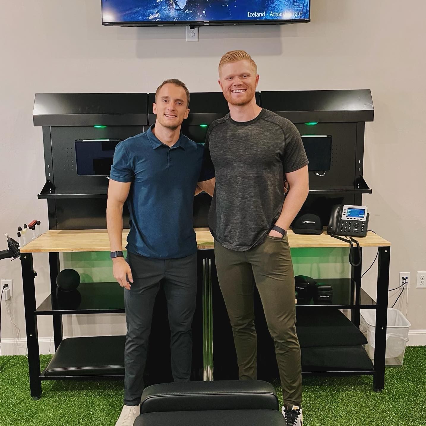 Two men standing in front of a large black aquarium setup, smiling indoors.