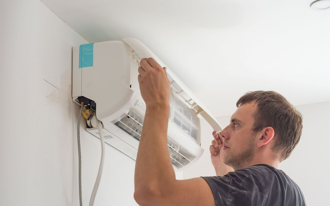 Technician inspecting a wall-mounted air conditioner filter with a ladder nearby