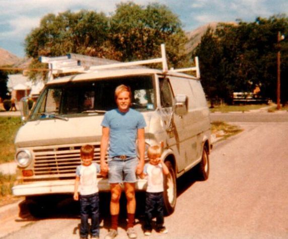 Man standing with two children beside a white van on a sunny residential street