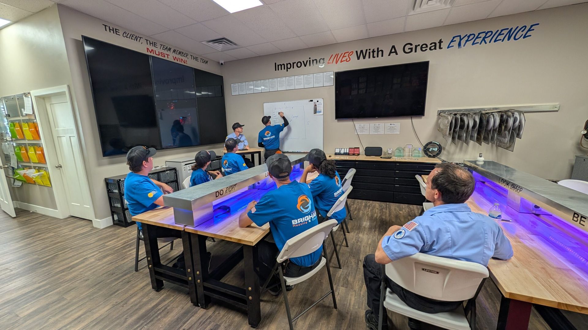 Meeting room with people seated around a long table, facing a wall-mounted TV.