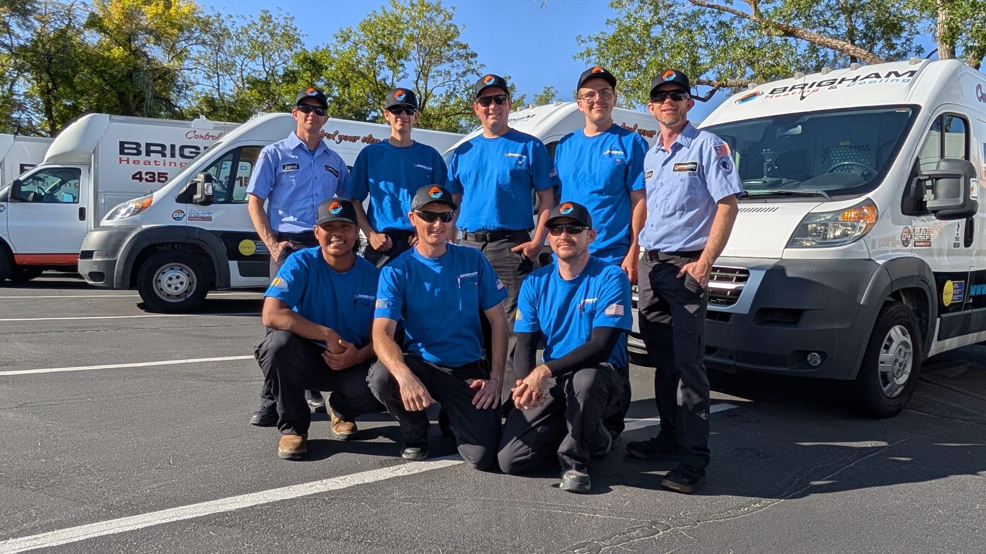 Group of workers in blue shirts posing in front of two white service vans in a parking lot