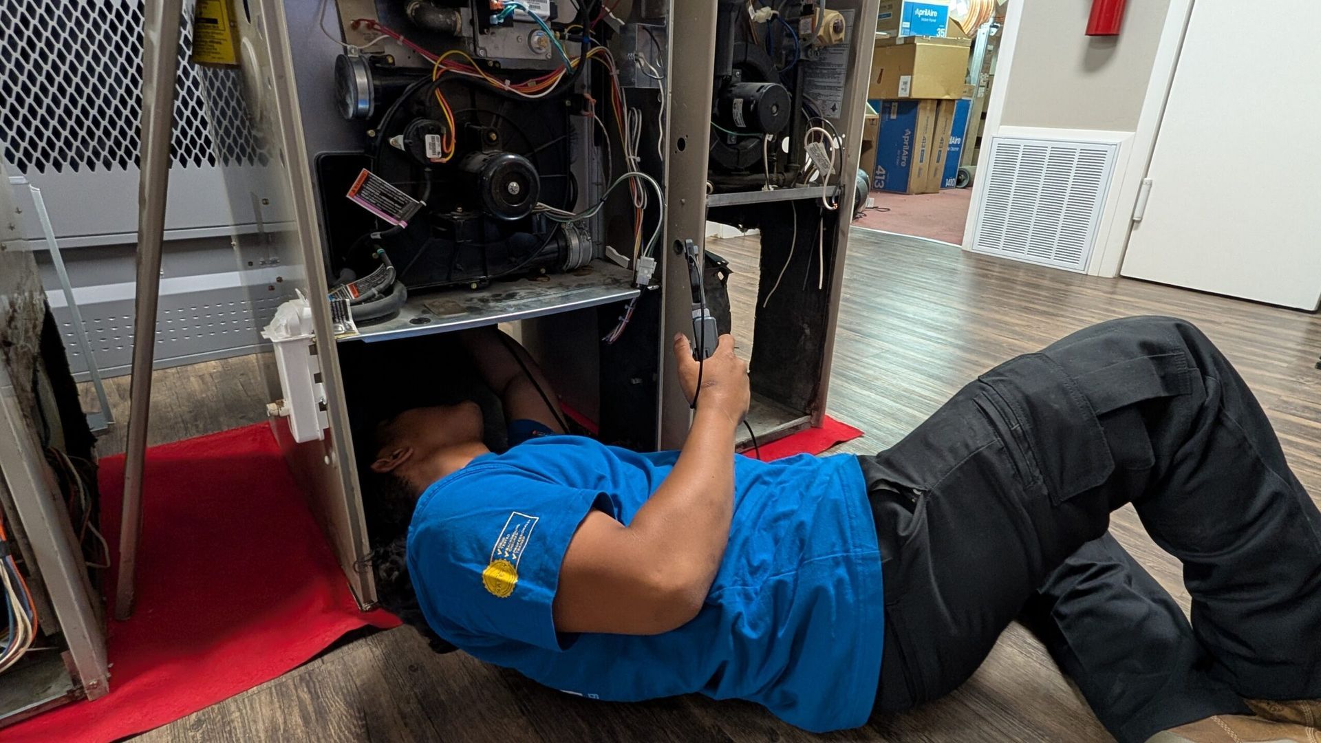 Technician lying under an open machine, inspecting wiring inside a workshop.