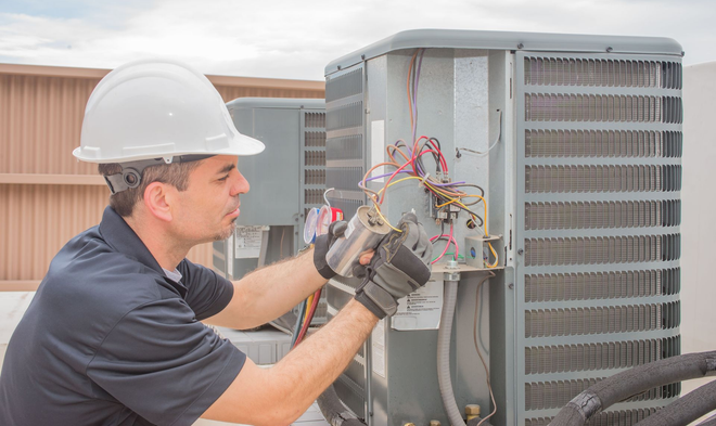 Technician in hard hat inspecting wiring on an outdoor HVAC unit
