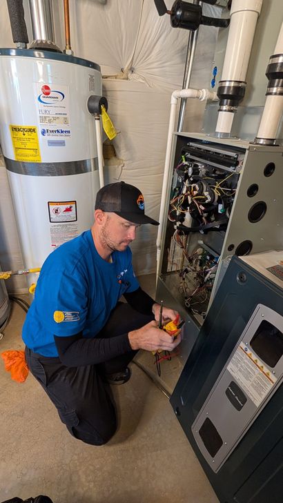 Technician kneeling beside a water heater, inspecting an open HVAC unit with tools in a utility room