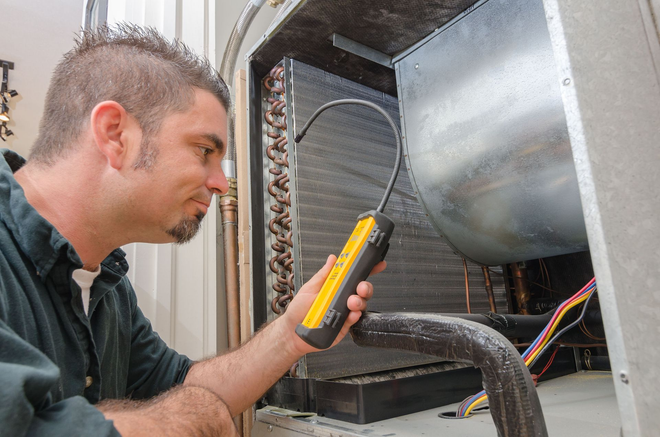 Technician inspecting HVAC unit with a multimeter inside a metal equipment cabinet