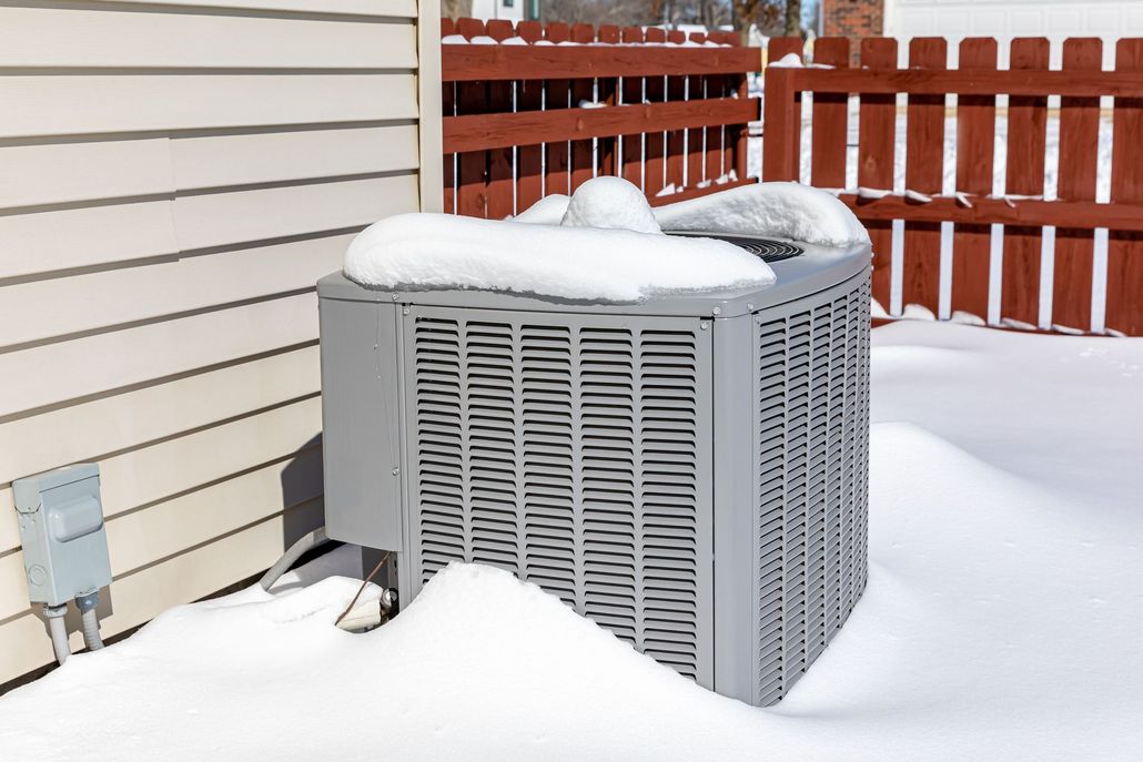 Snow-covered outdoor air conditioner beside a house and red fence