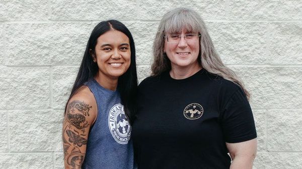 Two women are standing next to each other in front of a brick wall