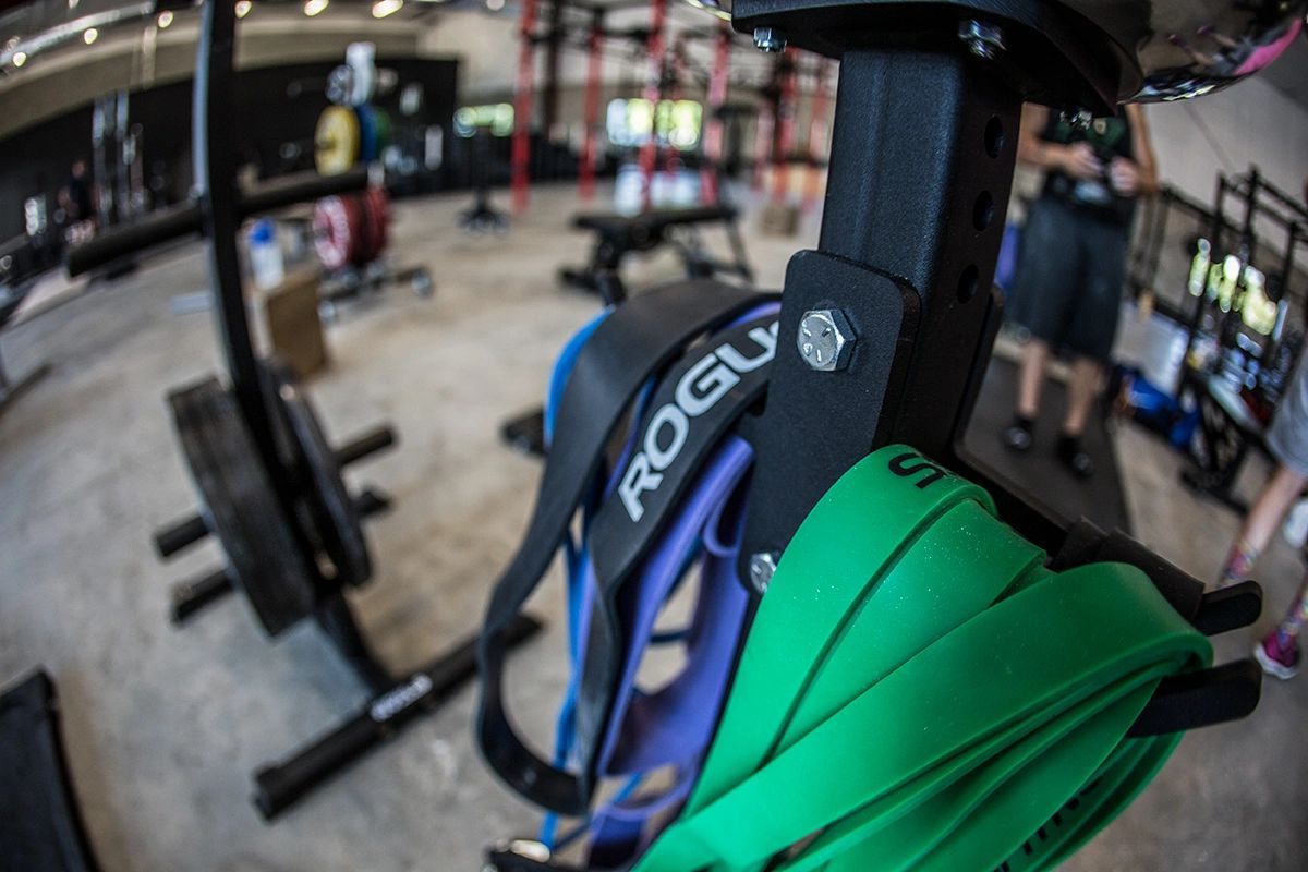 A green resistance band is hanging from a rogue machine in a gym.