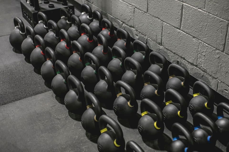 A row of kettlebells are lined up against a brick wall in a gym.